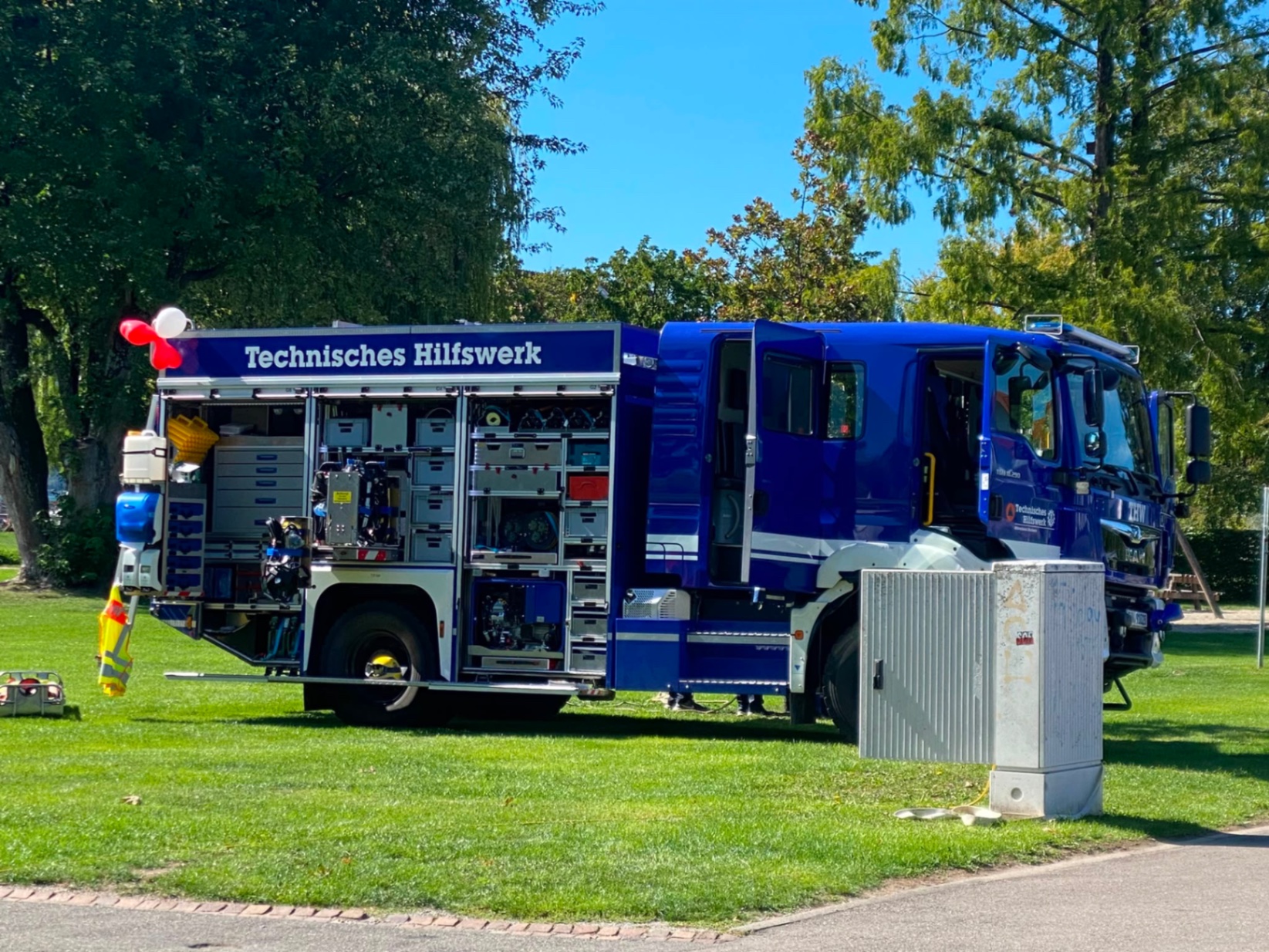 Das blaue Fahrzeug des Technischen Hilfswerks Stockach steht bei Sonnenschein auf der Rasenfläche im Uferpark Ludwigshafen, die Ladeschubladen mit Technik und Werkzeug sind ausgefahren.